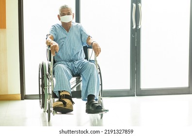 Senior Asian Male Patient Wearing A Mask Sits Sadly In A Wheelchair To Recuperate And See A Doctor In The Hospital.