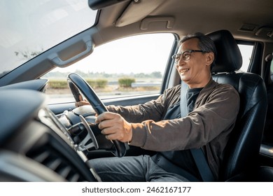 Senior Asian man drives a car vehicle on a clear day. With beautiful blue sky. He smiling driving to travel by car. Old man getting new car. - Powered by Shutterstock