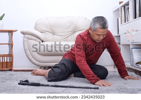 Senior Asian man falling down and lying on floor with wooden walking stick in living room.