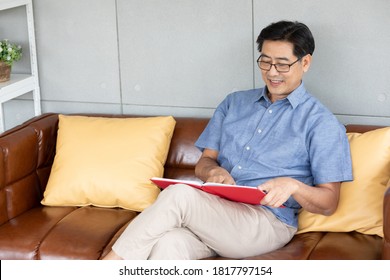 Senior Asian Man Reading Book On Sofa