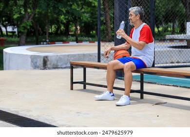 Senior Asian man in retirement age drinking water after playing basketball at outdoor court for healthy and fun activity to exercise and workout against aging illness - Powered by Shutterstock