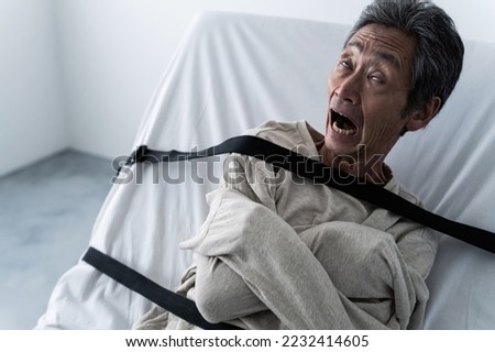 Senior Asian man strapped to bed.