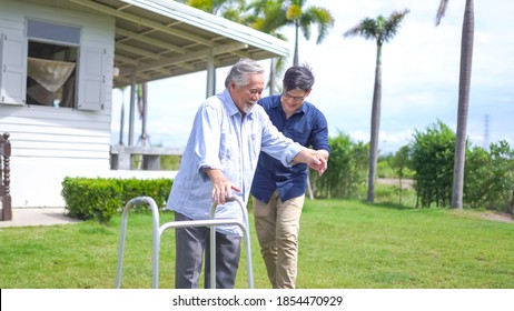 Senior Asian Man Struggling To Us A Walker. His Adult Son Is Helping Him