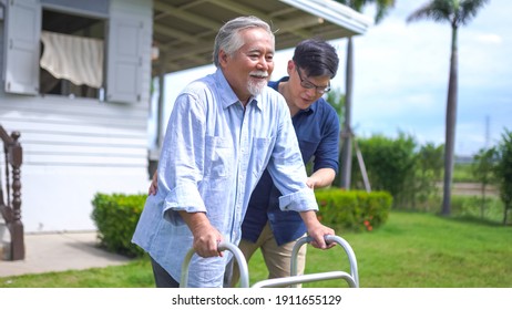 Senior Asian Man Struggling To Us A Walker. His Adult Son Is Helping Him