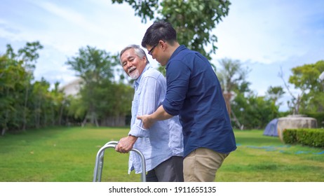 Senior Asian Man Struggling To Us A Walker. His Adult Son Is Helping Him