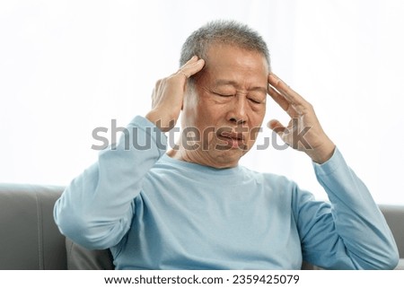Senior asian man suffering from a severe headache on the sofa, seeking relief, headache woes, migraine misery, head pain at home