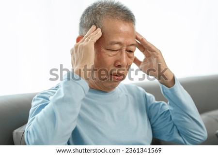 Senior asian man suffering from a severe headache on the sofa, seeking relief, headache woes, migraine misery, head pain at home