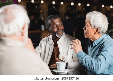 Senior Asian Man Talking And Gesturing During Meeting With Multiethnic Friends In Cafe