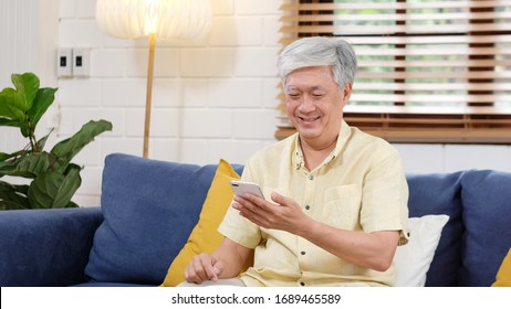 Senior Asian Man Using Mobile Phone At Home Living Room Background, Happy Retirement Asia Male Holding Smartphone While Sitting On Sofa, Active Old, Elderly People And Technology