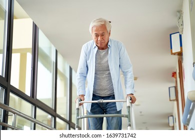 senior asian man walking using a walker in hallway of hospital or nursing home