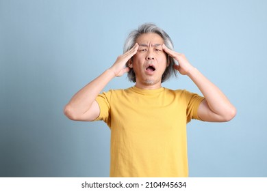 The senior Asian man with yellow t shirt standing on the blue background. - Shutterstock ID 2104945634
