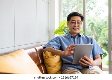 Senior Asian men at the sofa couch using smartphone tablet for browsing internet and reading news online in the morning. Technology with retirement relax lifestyle. - Powered by Shutterstock