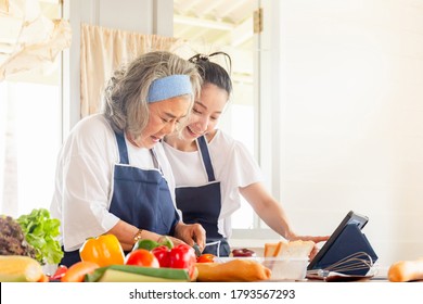 Senior Asian Mother And Middle Aged Daughter Cooking Together At Kitchen