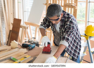 Senior Asian Old Man Carpenter Using Electric Wood Sanding Machine To Scrub Plank In Workshop