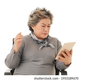 Senior Asian Old Woman Sitting On Chair, Holding And Looking Tablet Feeling Sad Or Angry On White Background.