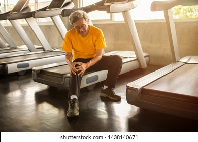 Senior Asian Sport Man Injury Knee Pain  Sitting On Treadmill In Fitness Gym . Aged  Suffering From Arthritis Elder Male Exercising , Workout, Training ,healthy ,Retirement ,older, With Copy Space