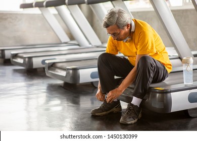 Senior Asian Sport Man Tying Shoelaces On Treadmill In Fitness Gym Ready Walking With Headphone And Water Bottle . Elder Male Exercising , Workout, Training ,healthy ,Retirement ,older