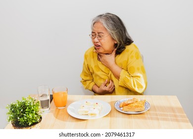 Senior asian woman with acid reflux problem, sore throat. While eating patty, food stuck in the throat, burning sensation in the esophagus, irritation, coughing, suffocation and difficulty swallowing.