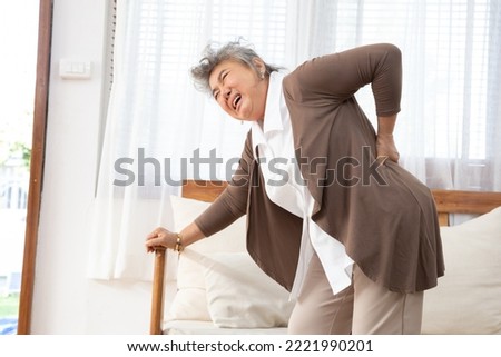 Senior Asian woman is bent over with her hand on the couch because she has lower back pain that is hurting, Osteoarthritis and spinal stenosis concept Stockfoto © 
