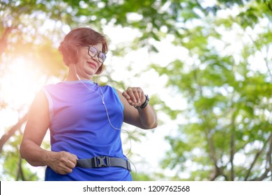 Senior asian woman checking time from smart watch. Checking heart rate while jogging in the park. Looking on smartwatch her heartbeat while running    - Powered by Shutterstock