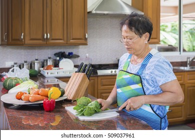 Senior Asian Woman Cutting Kale And Vegetables For Salad. Cooking And Home Concept