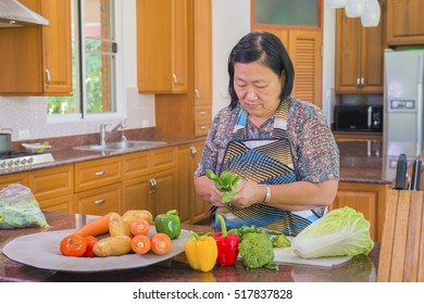 Senior Asian Woman Cutting Kale And Vegetables For Salad. Cooking And Home Concept