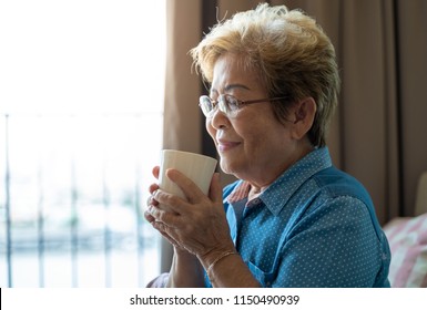 A senior asian woman is drinking a cup of coffee and feeling good smell of her coffee or tea - Powered by Shutterstock