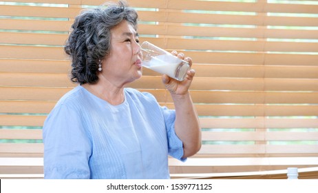 Senior Asian Woman Drinking Milk At Kitchen Home In The Morning, Elderly Asia Female Holding Glass Of Milk For Dairy Breakfast, Retirement People Healthy Lifestyle  