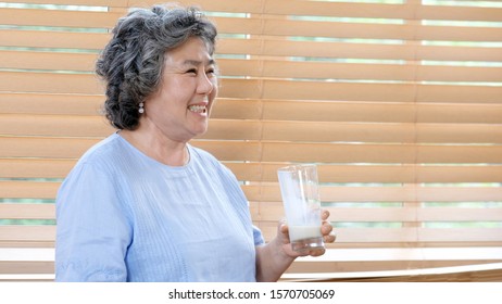 Senior Asian Woman Drinking Milk At Kitchen Home In The Morning, Elderly Asia Female Holding Glass Of Milk For Dairy Breakfast, Retirement People Healthy Lifestyle  