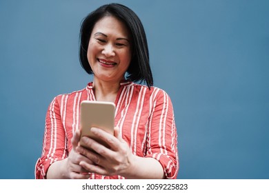 Senior Asian Woman Having Fun Using Mobile Phone Outdoor - Focus On Face