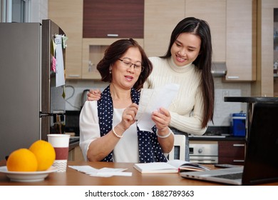 Senior Asian Woman And Her Adult Daughter Discussing Utility Bills They Need To Pay Online When Sitting At Kitchen Table