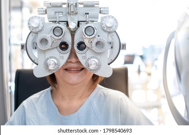 Senior Asian woman looking through optical phoropter during eye exam, diagnostic ophthalmology equipment, selective focus - Powered by Shutterstock