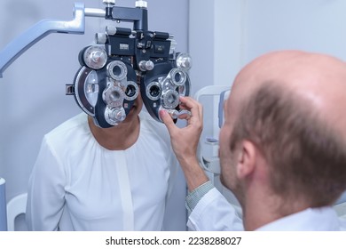 Senior Asian woman looking through optical phoropter during eye exam, diagnostic ophthalmology equipment, selective focus - Shutterstock ID 2238288027