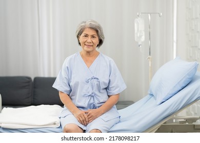 Senior Asian Woman Sitting On Bed With Receiving Saline Solution From Bag At Hospital Ward. Medicine, Health Care, Old People And Quarantine Concept