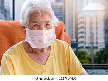 Senior Asian Woman Sitting Red Sofa Wear A Mask To Prevent COVID-19 Only In The Room.