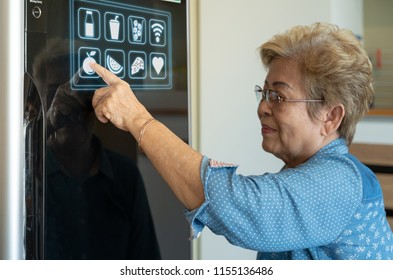 A senior asian woman is touching control panel of display on smart futuristic refrigerator