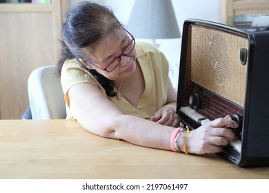 The Senior Asian Woman Trying To Listen Music From The Vintage Radio.