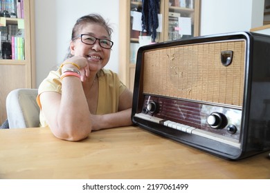 The Senior Asian Woman Trying To Listen Music From The Vintage Radio.