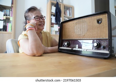 The Senior Asian Woman Trying To Listen Music From The Vintage Radio.