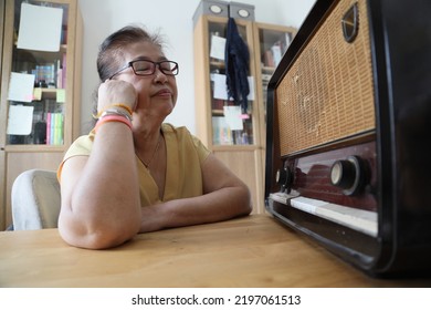 The Senior Asian Woman Trying To Listen Music From The Vintage Radio.