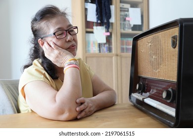 The Senior Asian Woman Trying To Listen Music From The Vintage Radio.