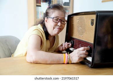 The Senior Asian Woman Trying To Listen Music From The Vintage Radio.