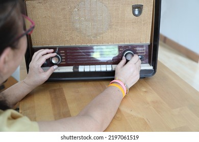 The Senior Asian Woman Trying To Listen Music From The Vintage Radio.