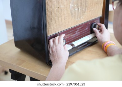 The Senior Asian Woman Trying To Listen Music From The Vintage Radio.