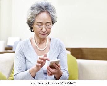 Senior Asian Woman Using Mobile Phone With Serious Facial Expression