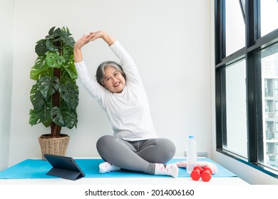 Senior Asian woman watching online courses on a laptop while exercising in the living room at home. Concept of workout training online. - Powered by Shutterstock