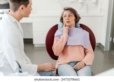 Senior attractive female patient touching cheek, having toothache, talking to professional doctor, sitting in dental chair in modern clinic. Concept of dental treatment, health care - Powered by Shutterstock