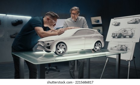 Senior automotive design engineers work on the prototype model of the car looking at the pencil sketches of the design. Using a rotary tool for final touch ups in the rake sculpture placed on a table. - Powered by Shutterstock