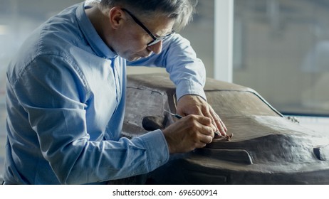 Senior Automotive Designer With Rake Sculpts Futuristic  Car Model From Plasticine Clay. He Works In A Special Studio Located In A Large Car Factory.