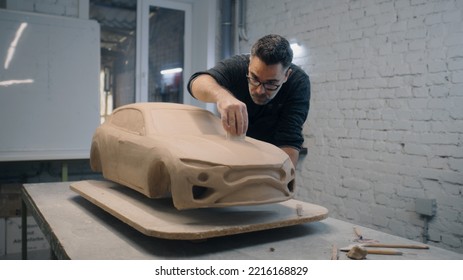 Senior automotive designer sculpts the prototype model of the car made of clay using sculpting tools. Experienced designer works in a workshop. Automotie industry. - Powered by Shutterstock